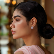 A person wearing pink stud earrings with a geometric design, set in silver.